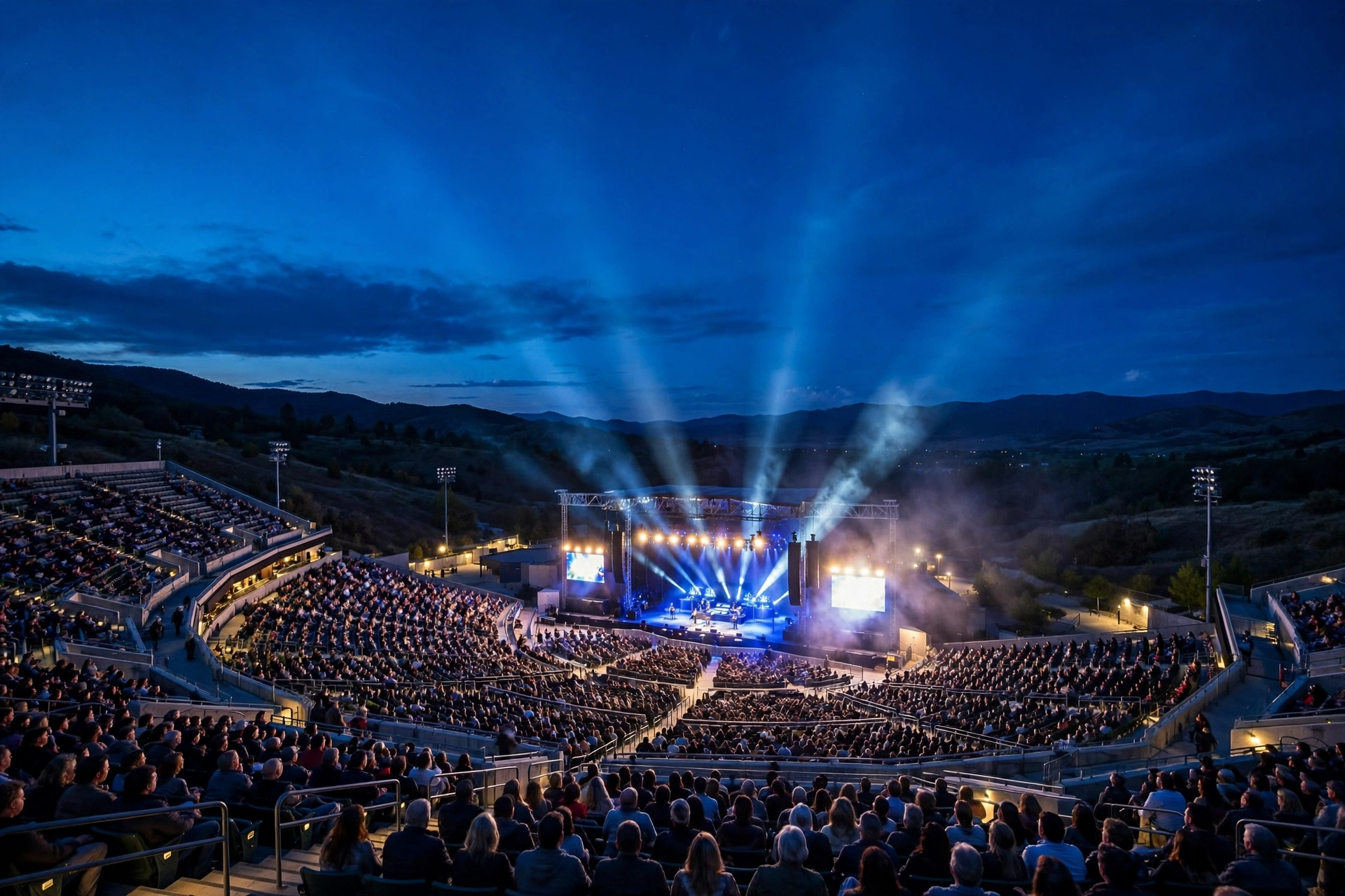 Large outdoor concert venue at blue hour filled with fans facing an illuminated stage